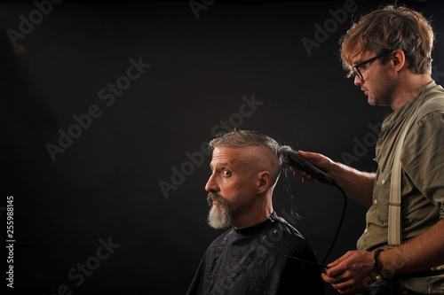 barber cuts a beard to a client to an elderly gray-haired man