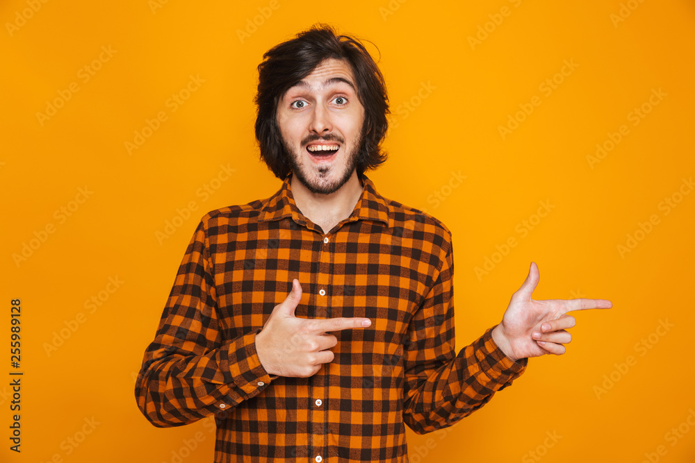 Handsome young happy man isolated over yellow wall background pointing.