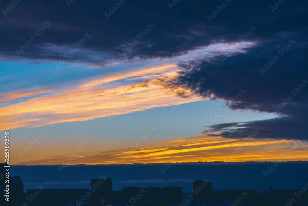 Cityscape with wonderful varicolored vivid dawn. Amazing dramatic blue cloud sky above dark silhouettes of city building roofs. Atmospheric background of orange sunrise in overcast weather. Copy space Cityscape with wonderful varicolored vivid dawn. Amazing dramatic blue cloud sky above dark silhouettes of city building roofs. Atmospheric background of orange sunrise in overcast weather. Copy space