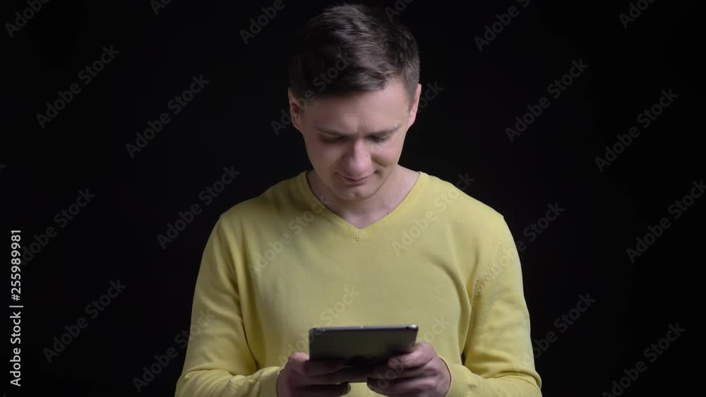 Portrait of middle-aged caucasian man in yellow sweater watching smilingly into tablet on black background. Portrait of middle-aged caucasian man in yellow sweater watching smilingly into tablet on black background.