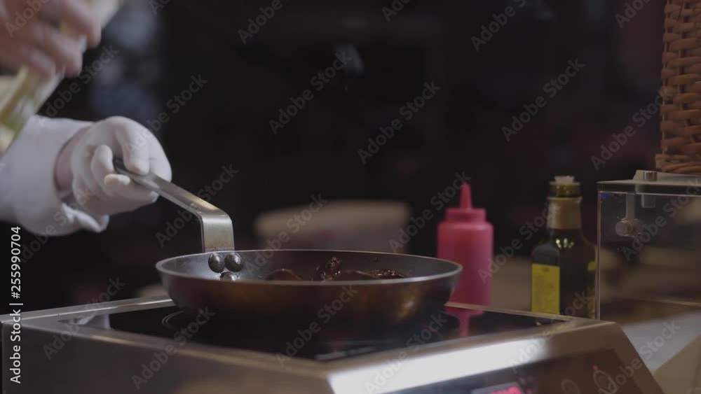 Hands of chef in white rubber gloves pouring white wine in the frying pan, cooking tasty dish in modern restaurant close up. Process of food preparing Hands of chef in white rubber gloves pouring white wine in the frying pan, cooking tasty dish in modern restaurant close up. Process of food preparing