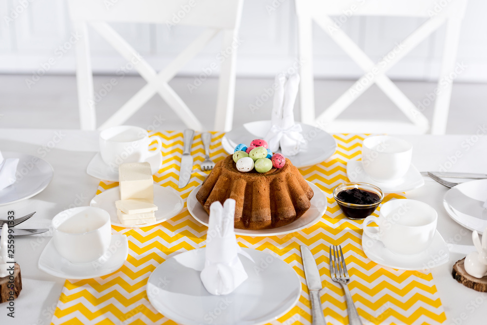 Easter cake with painted eggs and crockery on table