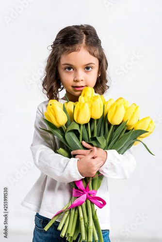 Front view of cute curly kid holding tulips bouquet on white