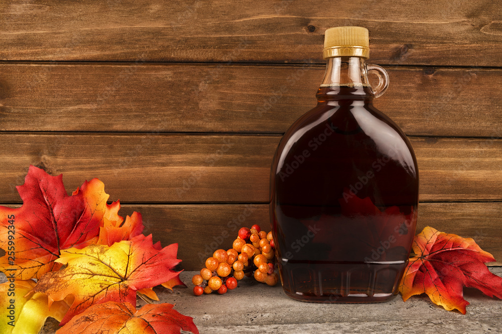 Maple syrup bottle on a wooden plank background. Maple leaves in