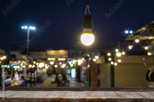 Wooden table in front of decorative outdoor string lights hanging on electricity post with blur people. Business  festival and holiday concepts  can used for display or montage your products.