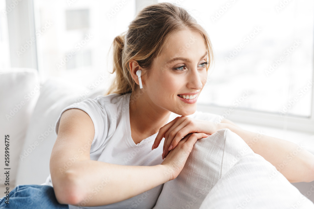 Portrait of charming girl wearing earpod smiling and sitting on couch in bright room at home Portrait of charming girl wearing earpod smiling and sitting on couch in bright room at home