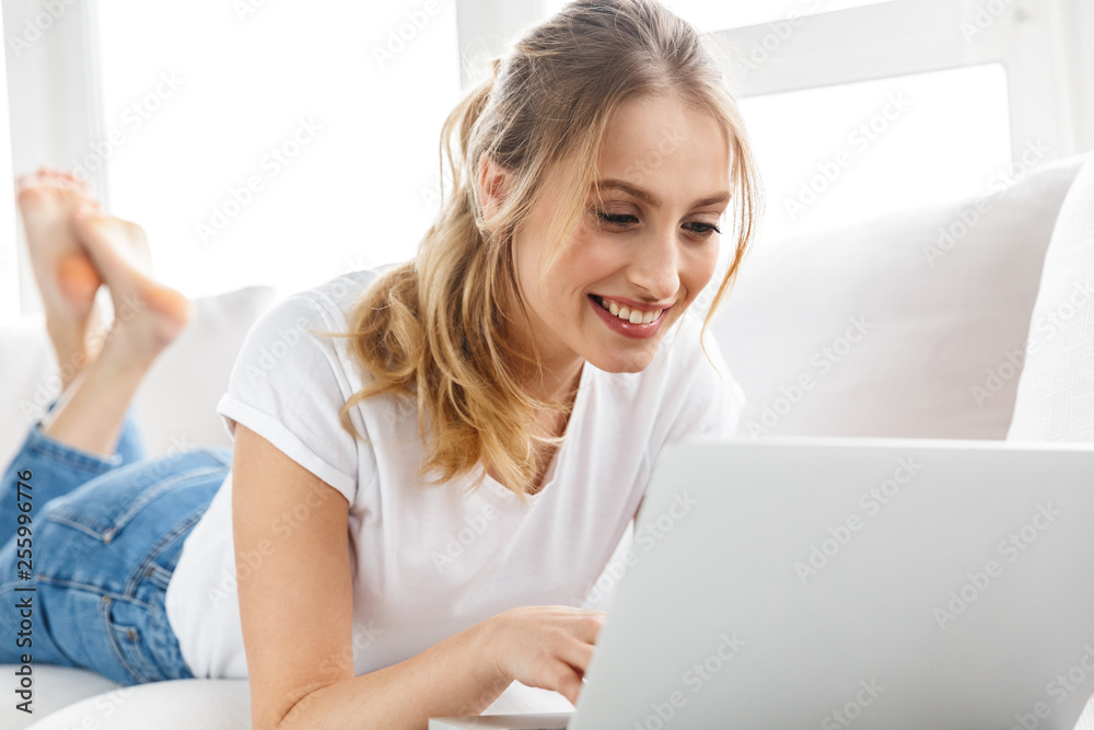 Portrait of gorgeous girl using laptop while lying on couch in bright room at home Portrait of gorgeous girl using laptop while lying on couch in bright room at home