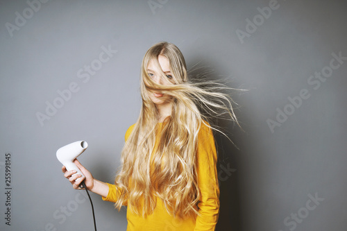 funny young blond woman blow-drying her long hair with blow dryer