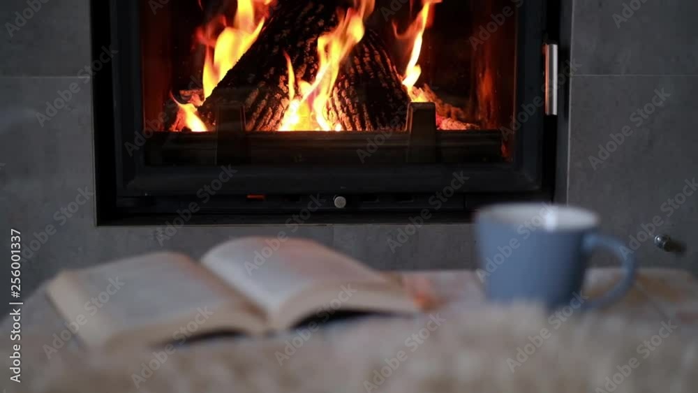 Hygge concept with open book and cup of tea near burning fireplace Hygge concept with open book and cup of tea near burning fireplace