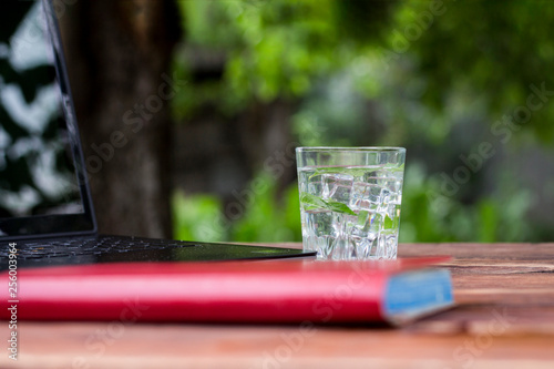Laptop, diary and a glass with a refreshing cold drink with ice cubes and mint leaves on a wooden table. The concept of work in nature, freelancing, work on vacation