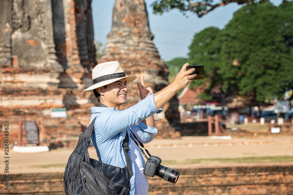 Tourists are shooting self portrait. Selfie portrait. Travel and tourism. Young caucasian man walk in the morning at temple in old city of Ayutthaya in Thailand.