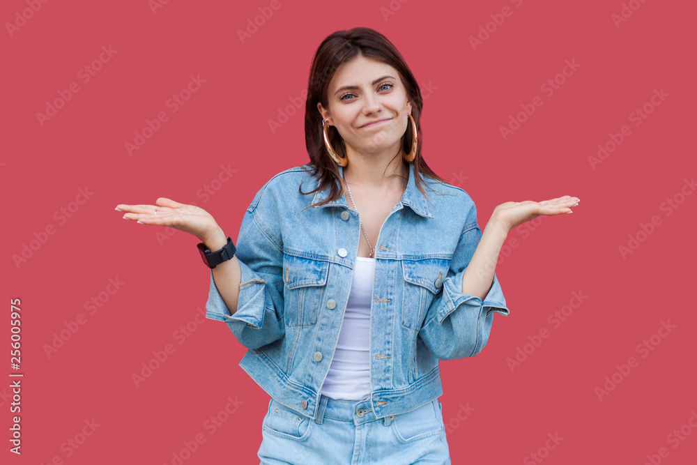 I don't know. Portrait of confused beautiful brunette young woman in denim casual style standing and looking at camera with raised arms and puzzled. indoor studio shot, isolated on red background. I don't know. Portrait of confused beautiful brunette young woman in denim casual style standing and looking at camera with raised arms and puzzled. indoor studio shot, isolated on red background.