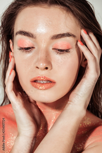 beautiful stylish young woman with coral glitter makeup posing and touching face