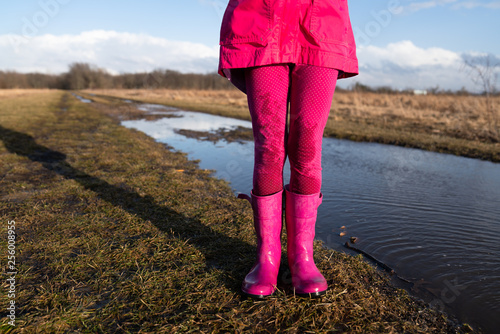 Low section of girl wearing rubber boots standing by puddle