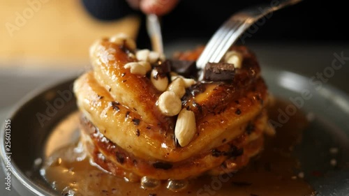 Tasty eating pancakes with sweet syrup and nuts in cafe using knife and fork photo