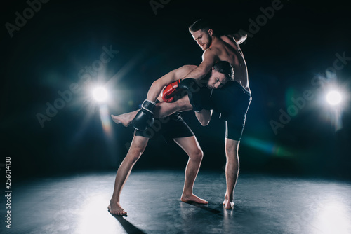 Fotografie barefoot strong muscular mma fighter in boxing gloves clinching another while sp