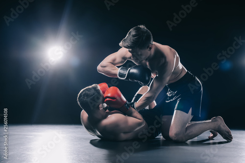Bild auf Leinwand Shirtless strong mma fighter in boxing gloves standing on knees above opponent a