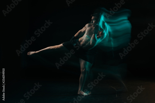 long exposure of shirtless muscular sportsman doing kick in green light on black © LIGHTFIELD STUDIOS