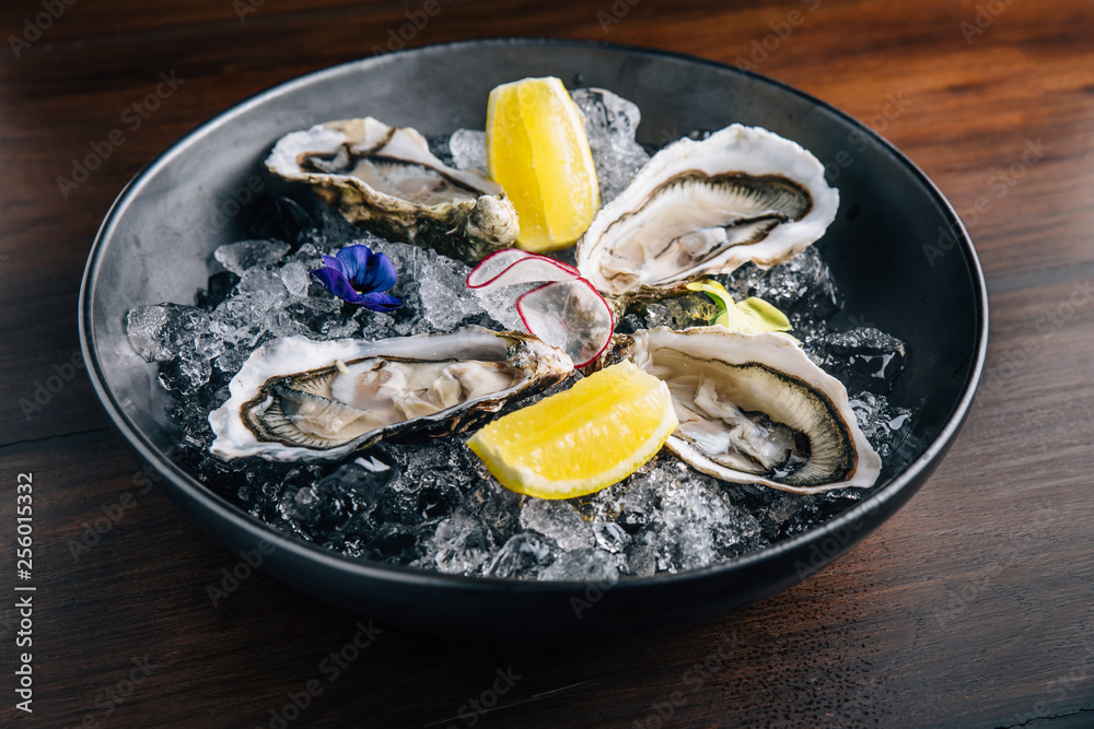 Fine de Claire Oyster and lemon served in black bowl with ice on wooden table.