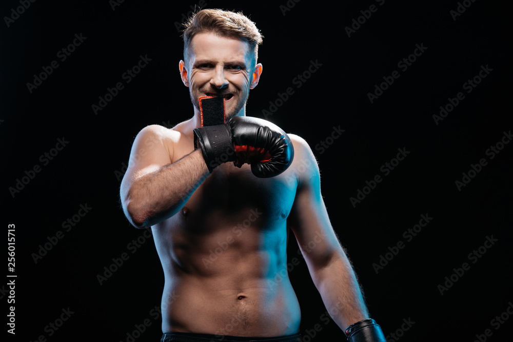 muscular sporty boxer taking off  boxing gloves with mouth isolated on black