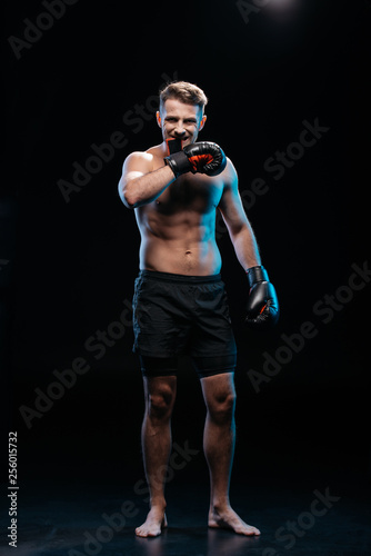 muscular barefoot sporty boxer taking off  boxing gloves with mouth on black © LIGHTFIELD STUDIOS