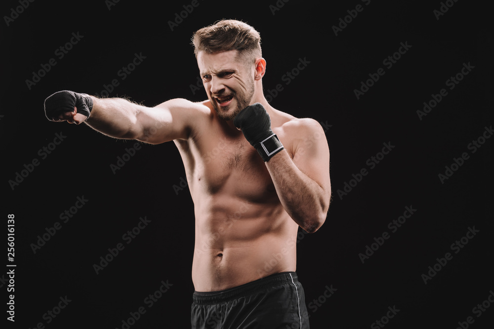 strenuous muscular mma fighter in bandages doing punch isolated on black