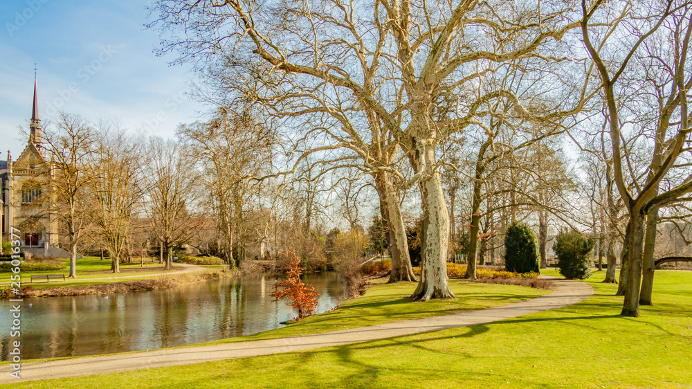 Beautiful view of a park with a pond, a path, trees and green grass and a church in the background, wonderful sunny winter day in Meerssen South Limburg in the Netherlands Holland