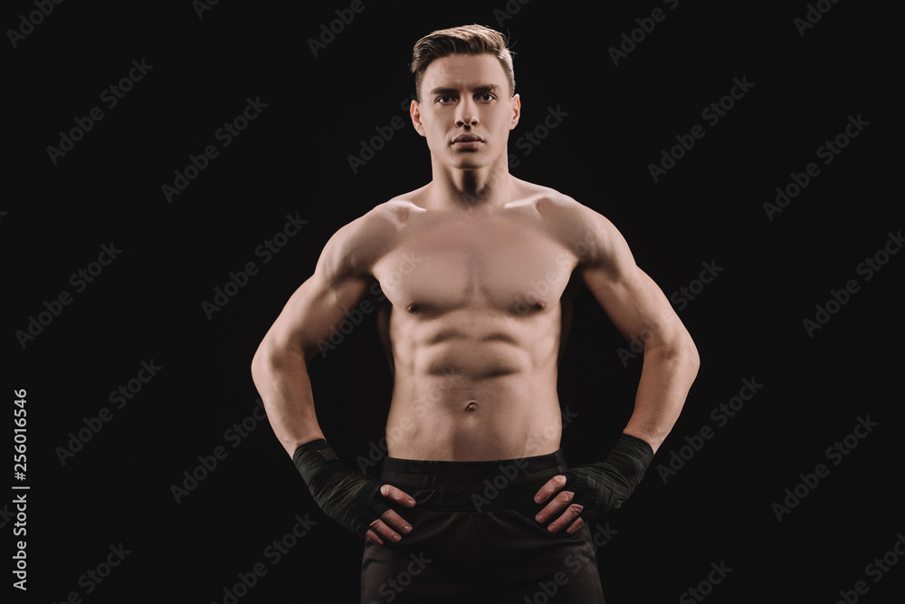 strong muscular sportsman looking at camera with hands on hips isolated on black