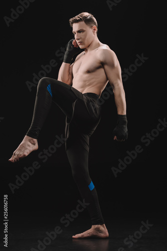 strong muscular barefoot sportsman in bandages doing kick on black