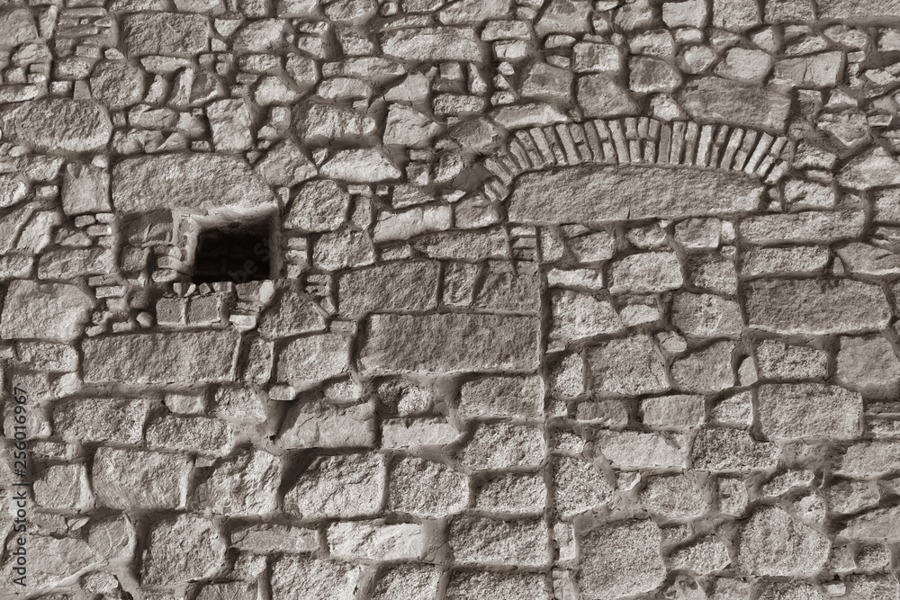 Medieval stone wall of the fortress with a small barred window Medieval stone wall of the fortress with a small barred window