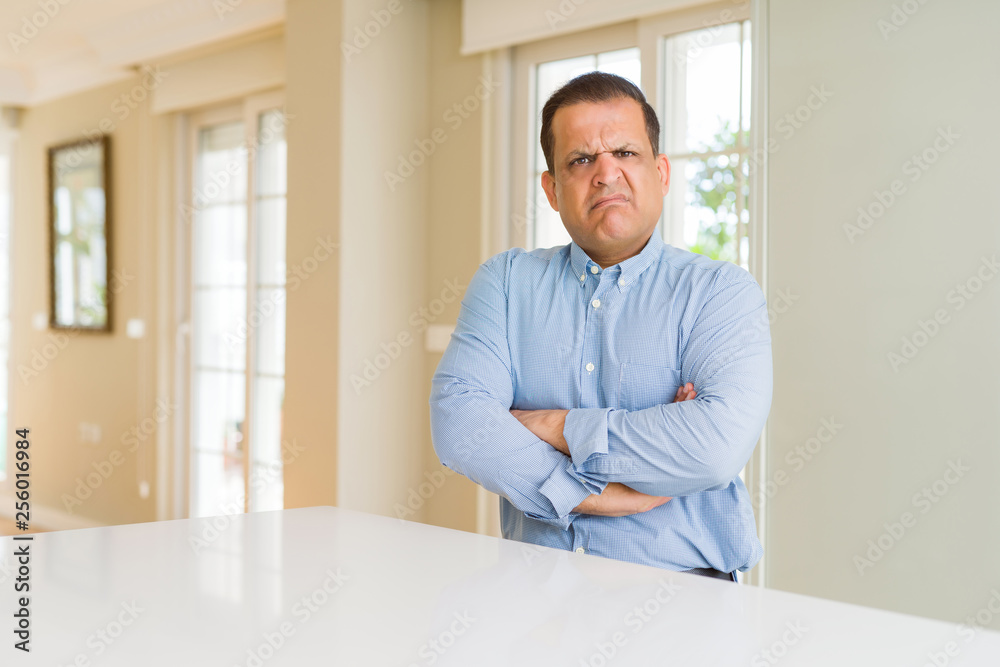 Middle age man sitting at home skeptic and nervous, disapproving expression on face with crossed arms. Negative person.
