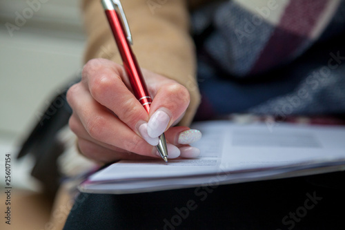 An image of a hand and pen completing a form. Woman hands with pastel manicure with pen.
