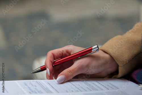 An image of a hand and pen completing a form. Woman hands with pastel manicure with pen.