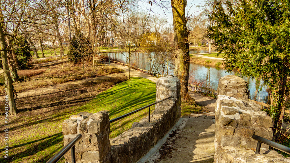 Part of the stone bridge in Proosdij public park with a view of small river and bare trees in the background, against blue sky, sunny winter day in Meerssen, South Limburg, Netherlands Part of the stone bridge in Proosdij public park with a view of small river and bare trees in the background, against blue sky, sunny winter day in Meerssen, South Limburg, Netherlands