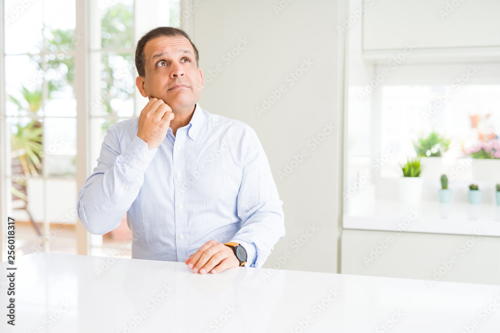 Middle age man sitting at home with hand on chin thinking about question, pensive expression. Smiling with thoughtful face. Doubt concept. Middle age man sitting at home with hand on chin thinking about question, pensive expression. Smiling with thoughtful face. Doubt concept.