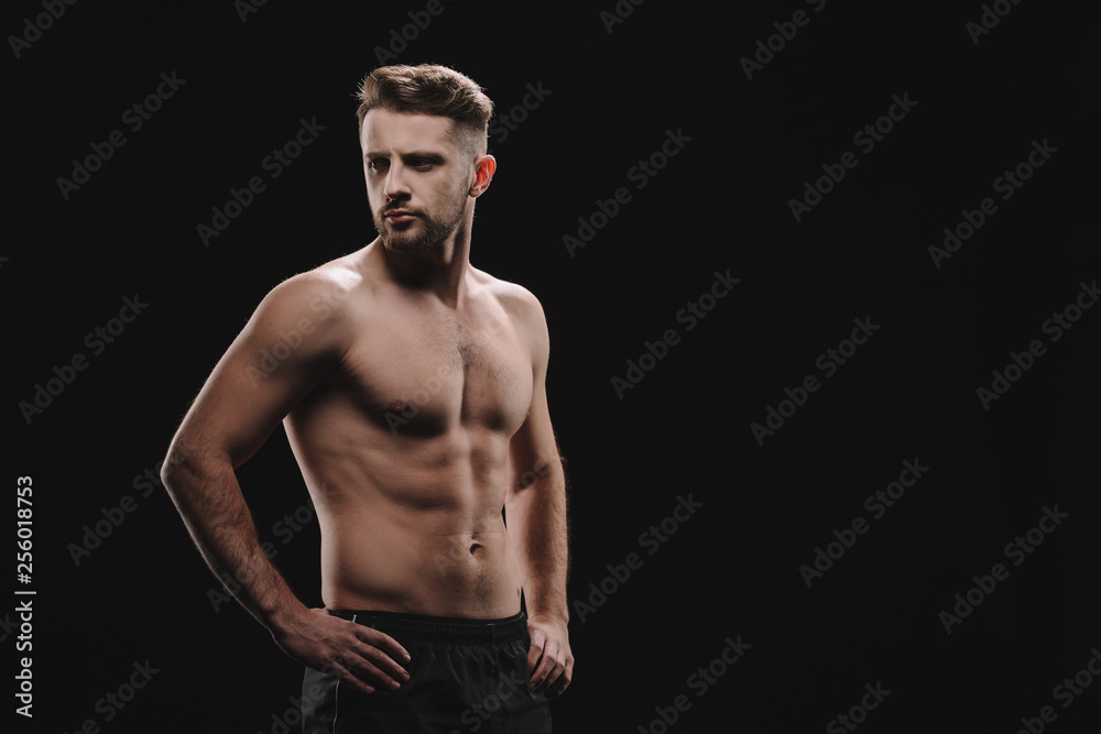 strong athletic muscular sportsman with hands on hips looking away isolated on black