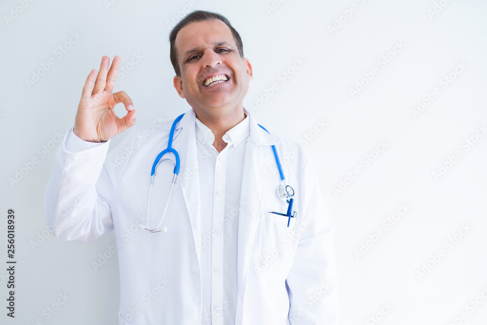 Middle age doctor man wearing stethoscope and medical coat over white background smiling positive doing ok sign with hand and fingers. Successful expression. Middle age doctor man wearing stethoscope and medical coat over white background smiling positive doing ok sign with hand and fingers. Successful expression.