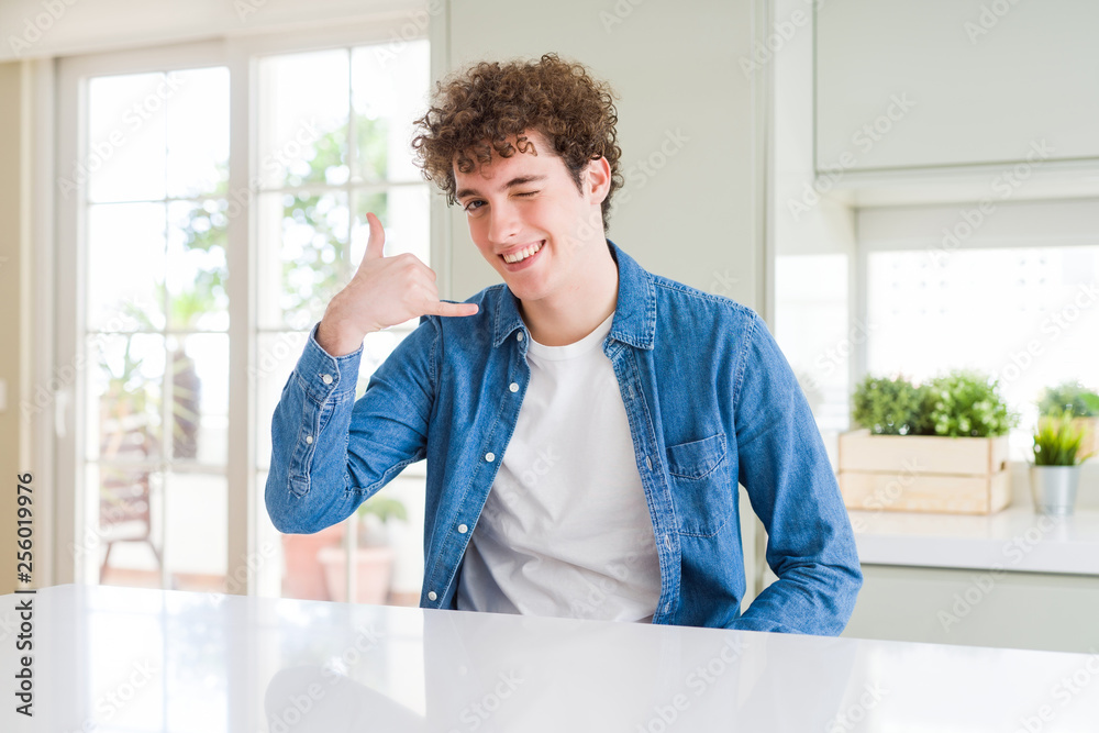 Young handsome man wearing casual denim jacket at home smiling doing phone gesture with hand and fingers like talking on the telephone. Communicating concepts.
