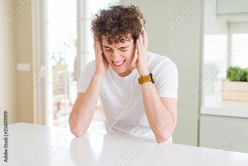 Young man listening to music wearing headphones at homes suffering from headache desperate and stressed because pain and migraine. Hands on head. © Krakenimages.com