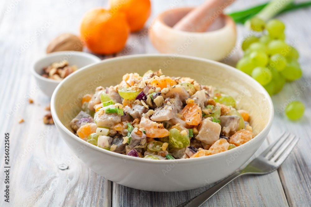 Salad with herring, tangerines, grapes, onions and walnuts in bowl on wooden table. Selective focus.