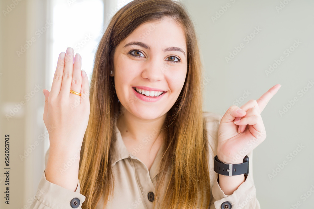 Beautiful young woman showing alliance ring on hand very happy pointing with hand and finger to the side Beautiful young woman showing alliance ring on hand very happy pointing with hand and finger to the side