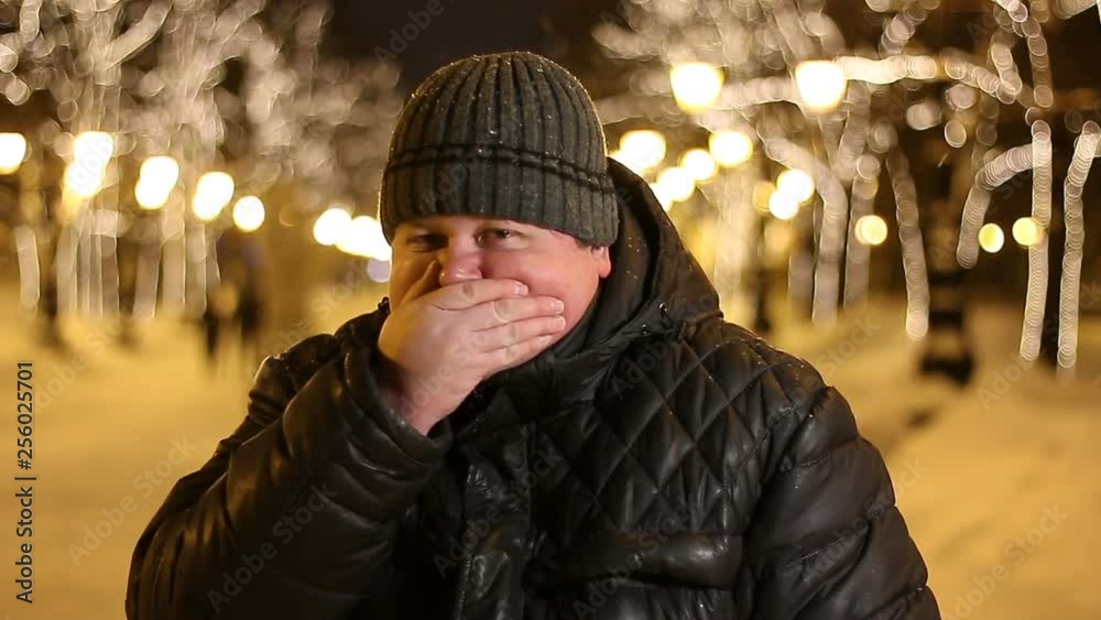 Young fat man feels nauseous and closes his mouth outdoors on a winter night, Young fat man feels nauseous and closes his mouth outdoors on a winter night,