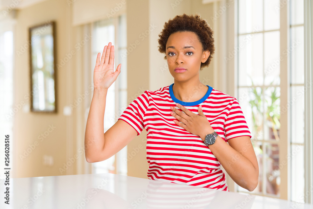 Young beautiful african american woman at home Swearing with hand on chest and open palm, making a loyalty promise oath Young beautiful african american woman at home Swearing with hand on chest and open palm, making a loyalty promise oath