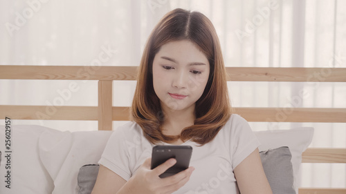 Young Asian woman using smartphone while lying on bed after wake up in the morning, Beautiful attractive Japanese girl smiling relax in bedroom at home. Enjoying time lifestyle women at home concept.
