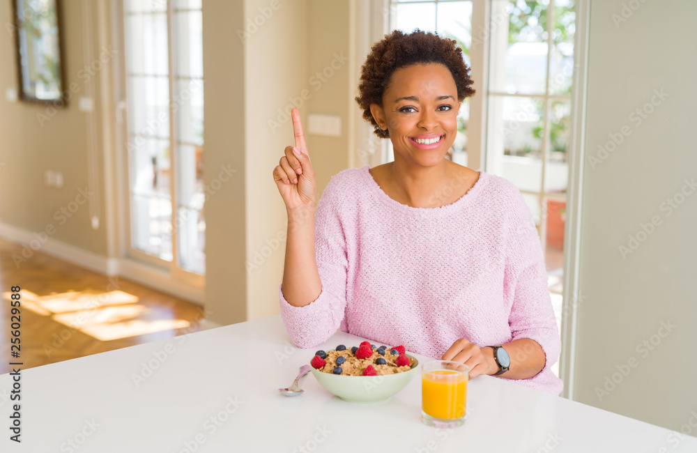Young african american woman having healthy breakfast in the morning at home showing and pointing up with finger number one while smiling confident and happy. Young african american woman having healthy breakfast in the morning at home showing and pointing up with finger number one while smiling confident and happy.