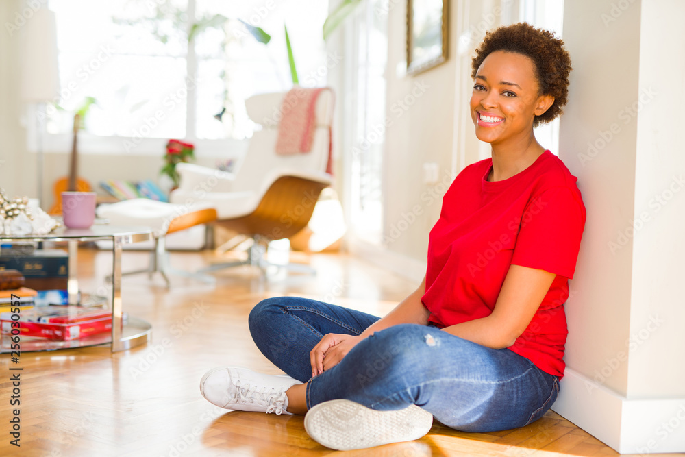 Beautiful young african american woman smiling confident to the camera showing teeth sitting on the floor at home Beautiful young african american woman smiling confident to the camera showing teeth sitting on the floor at home