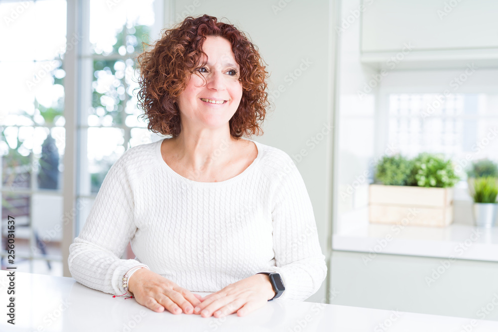 Beautiful senior woman wearing white sweater at home looking away to side with smile on face, natural expression. Laughing confident. Beautiful senior woman wearing white sweater at home looking away to side with smile on face, natural expression. Laughing confident.