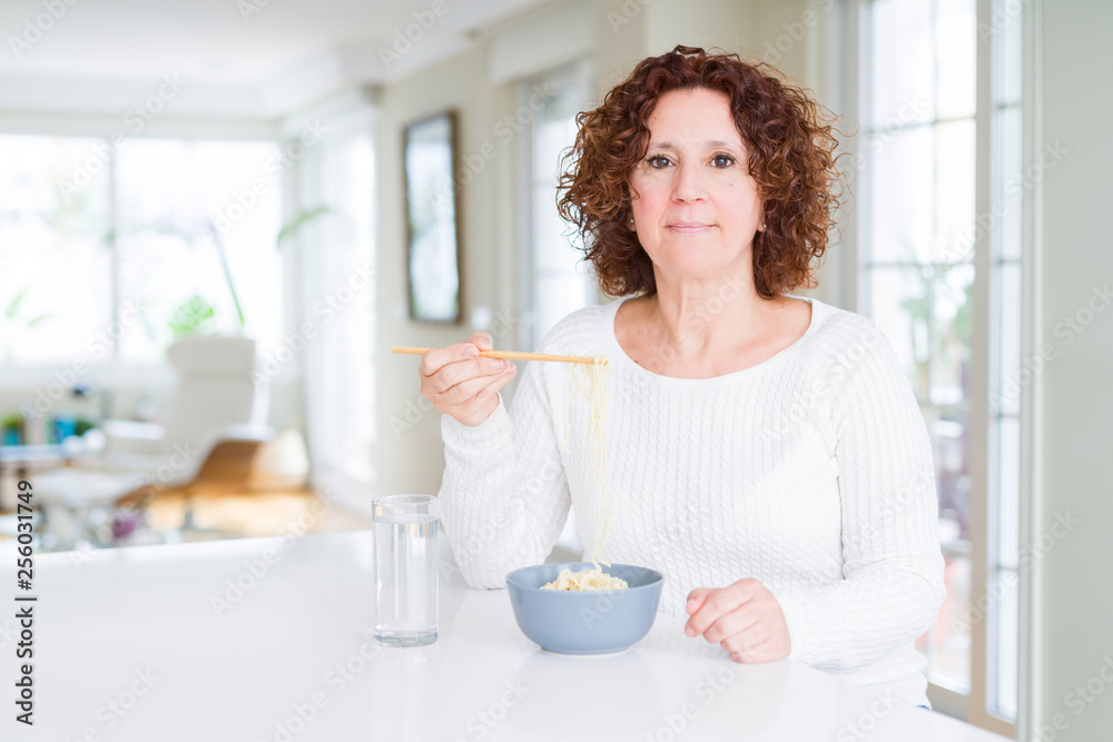 Senior woman eating asian noodles using chopsticks with a confident expression on smart face thinking serious Senior woman eating asian noodles using chopsticks with a confident expression on smart face thinking serious
