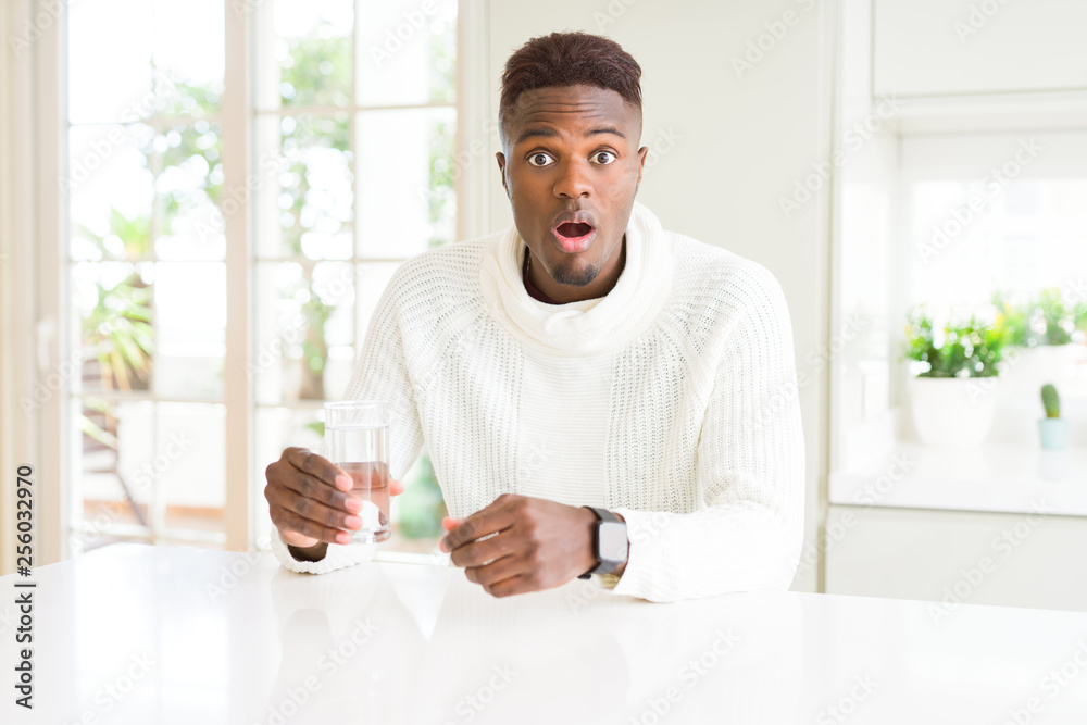 African american man driking a fresh glass of water scared in shock with a surprise face, afraid and excited with fear expression African american man driking a fresh glass of water scared in shock with a surprise face, afraid and excited with fear expression