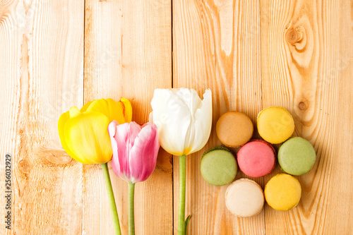 Colorful macaroons with tulips on wooden background 